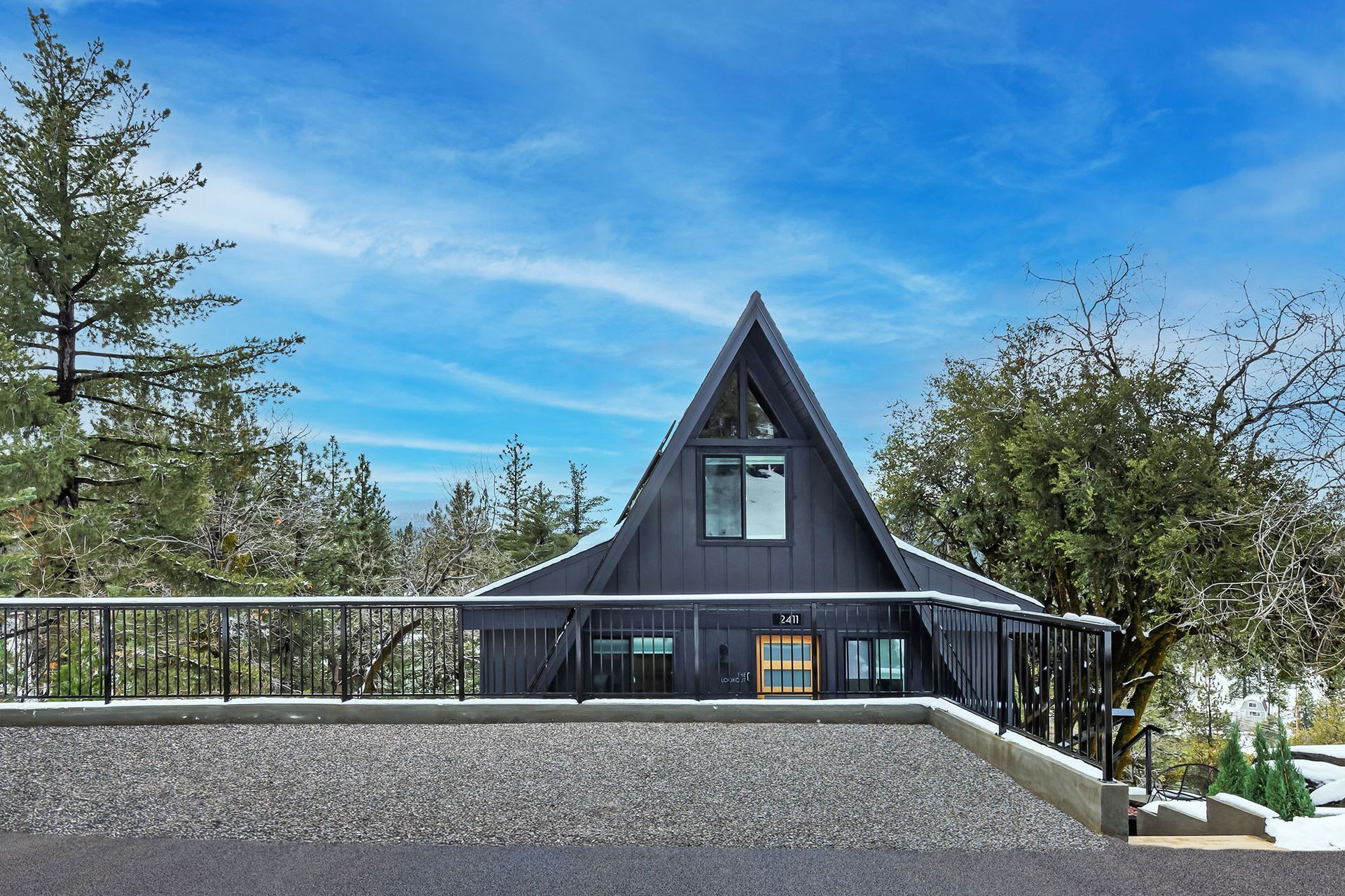 A black a frame house with a balcony and trees in the background