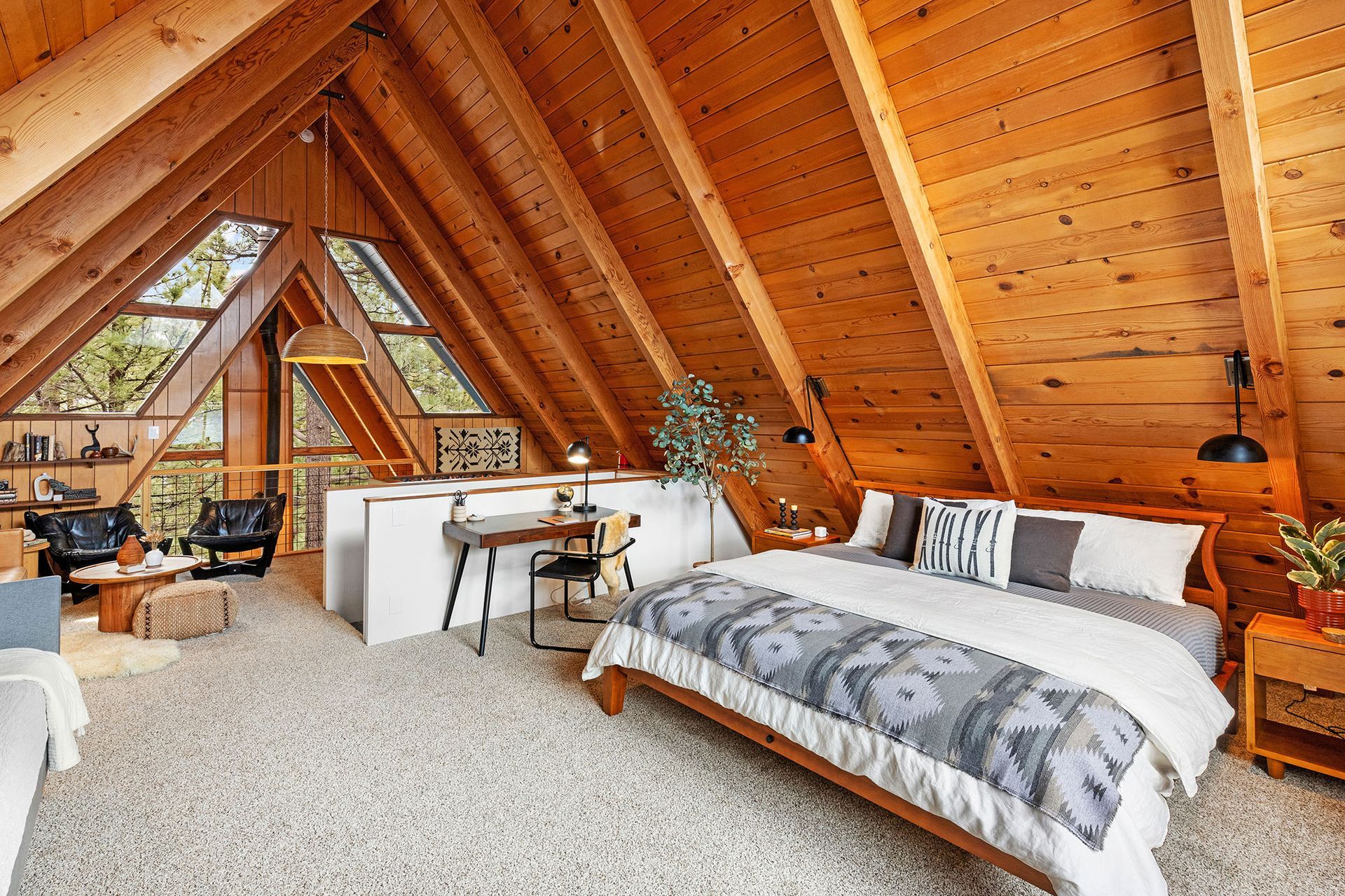 A bedroom in an attic with a king size bed and a desk.