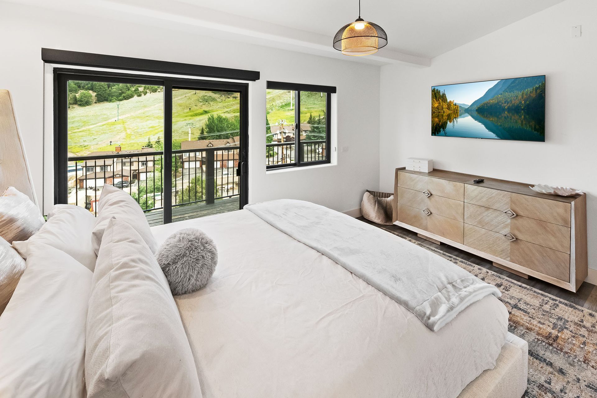 A bedroom with a king size bed , dresser , and large windows.