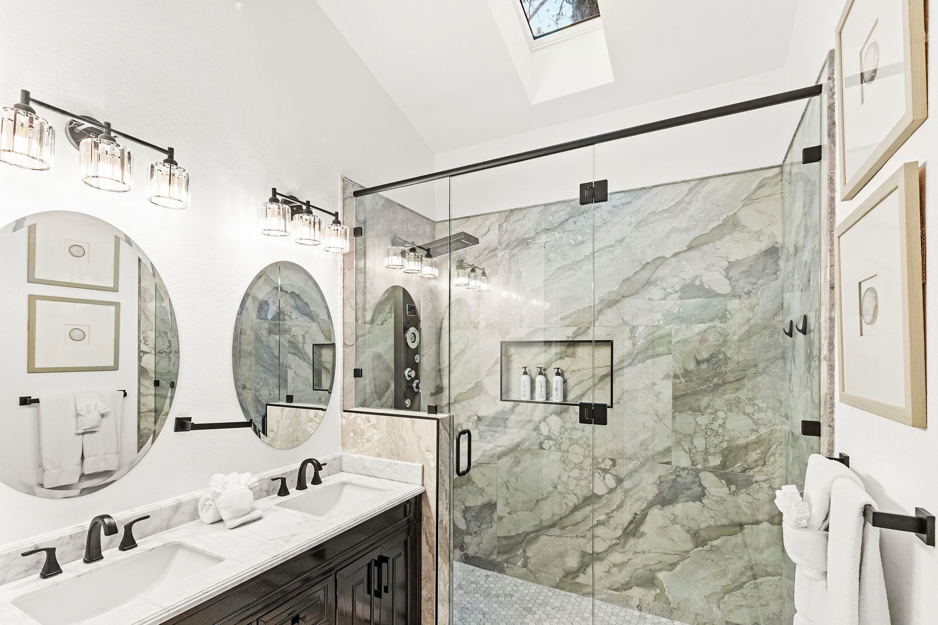 A bathroom with two sinks , a walk in shower and a skylight.