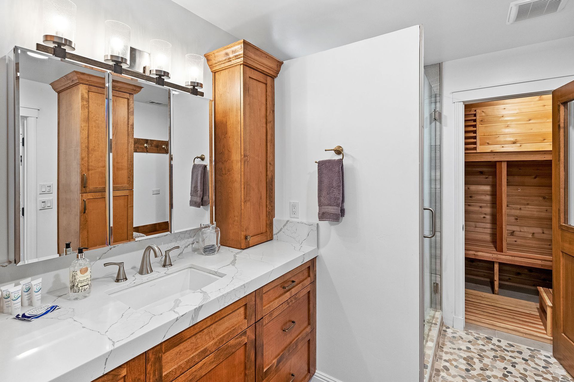 A bathroom with a double sink , mirror , cabinets and a sauna.