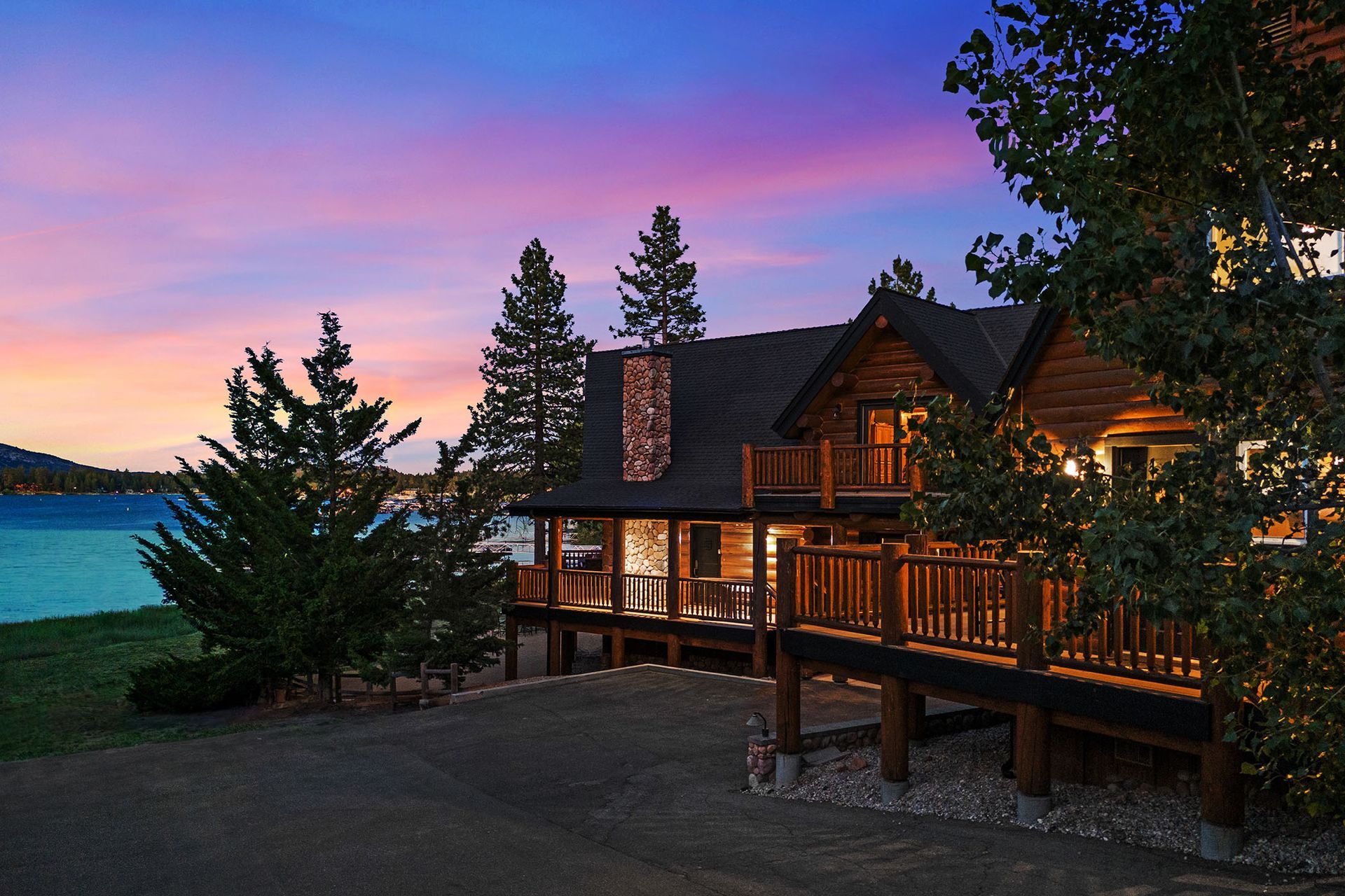 A large log cabin with a large deck overlooking a lake at sunset.
