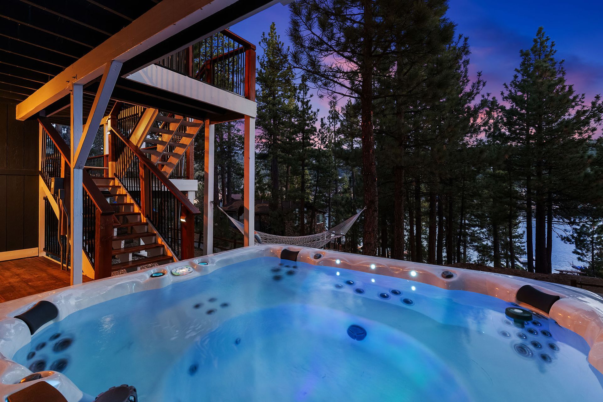 A large hot tub is sitting on top of a wooden deck surrounded by trees.