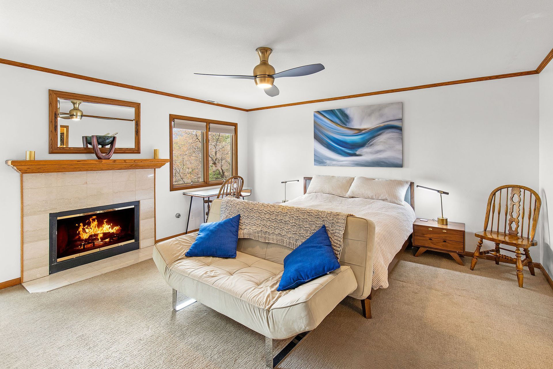 A bedroom with a bed , couch , fireplace and ceiling fan.