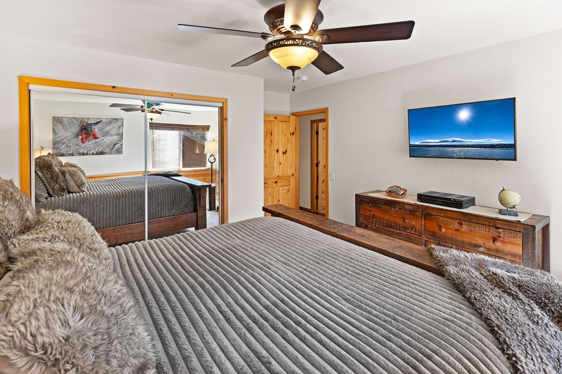 A bedroom with a large bed , ceiling fan , television and mirror.
