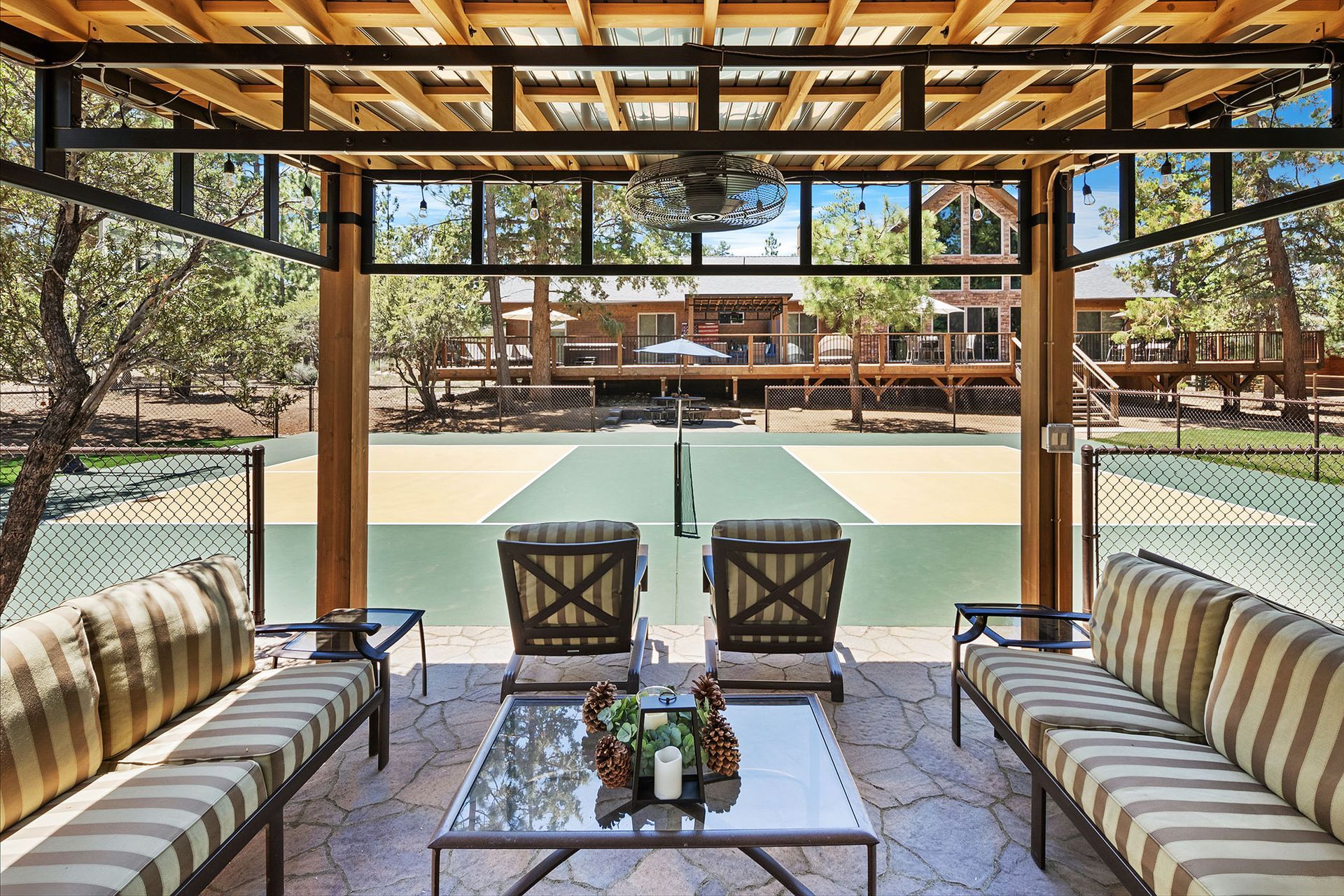 A patio with a table and chairs under a pergola with a basketball court in the background.