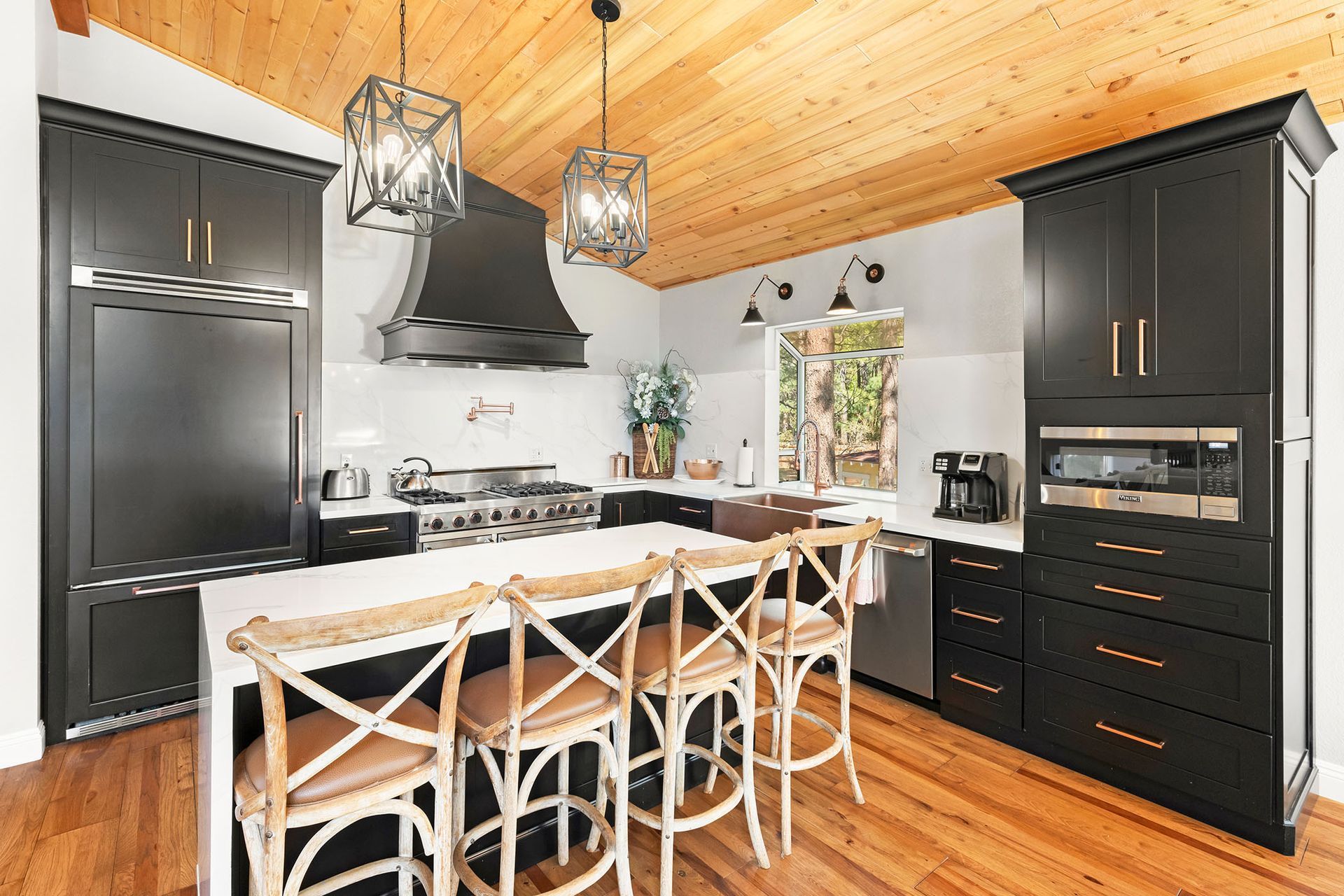 A kitchen with black cabinets and stainless steel appliances and a wooden ceiling.