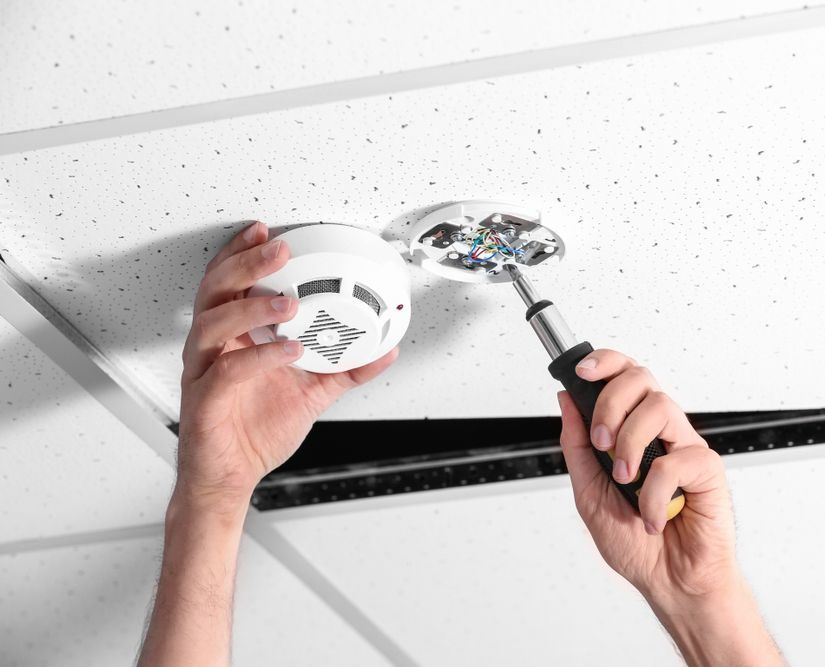 A Person Is Installing A Smoke Detector On The Ceiling — Keany's Electrical Service In North Nowra, NSW