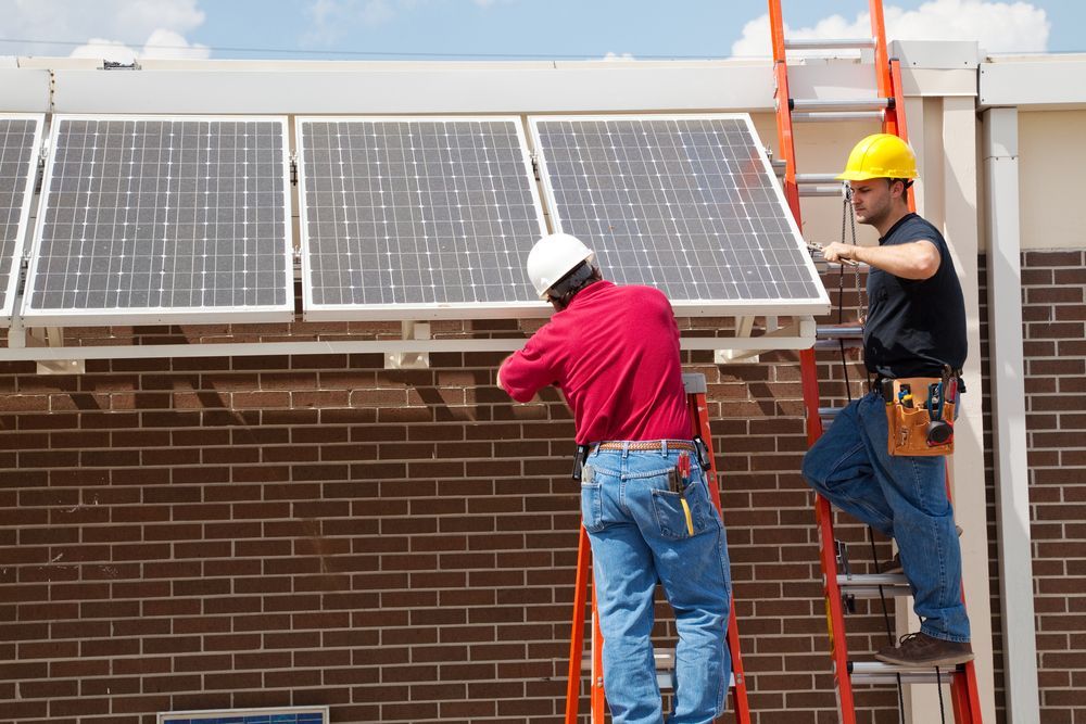 Two Men Are Installing Solar Panels On A Brick Building — Keany's Electrical Service In North Nowra, NSW