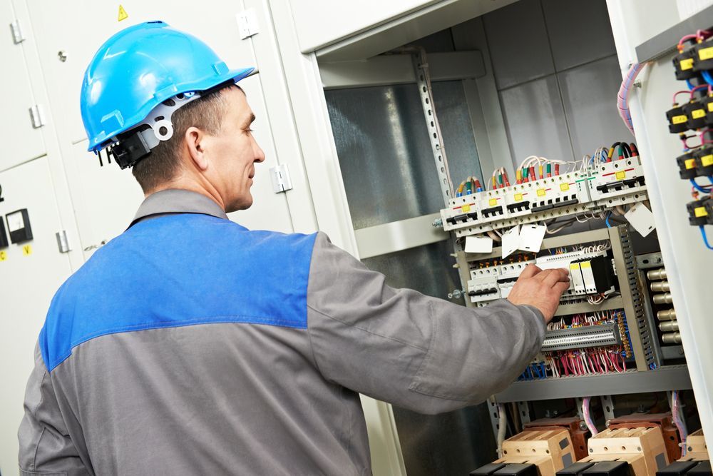 A Man Wearing A Hard Hat Is Working On An Electrical Panel — Keany's Electrical Service In North Nowra, NSW