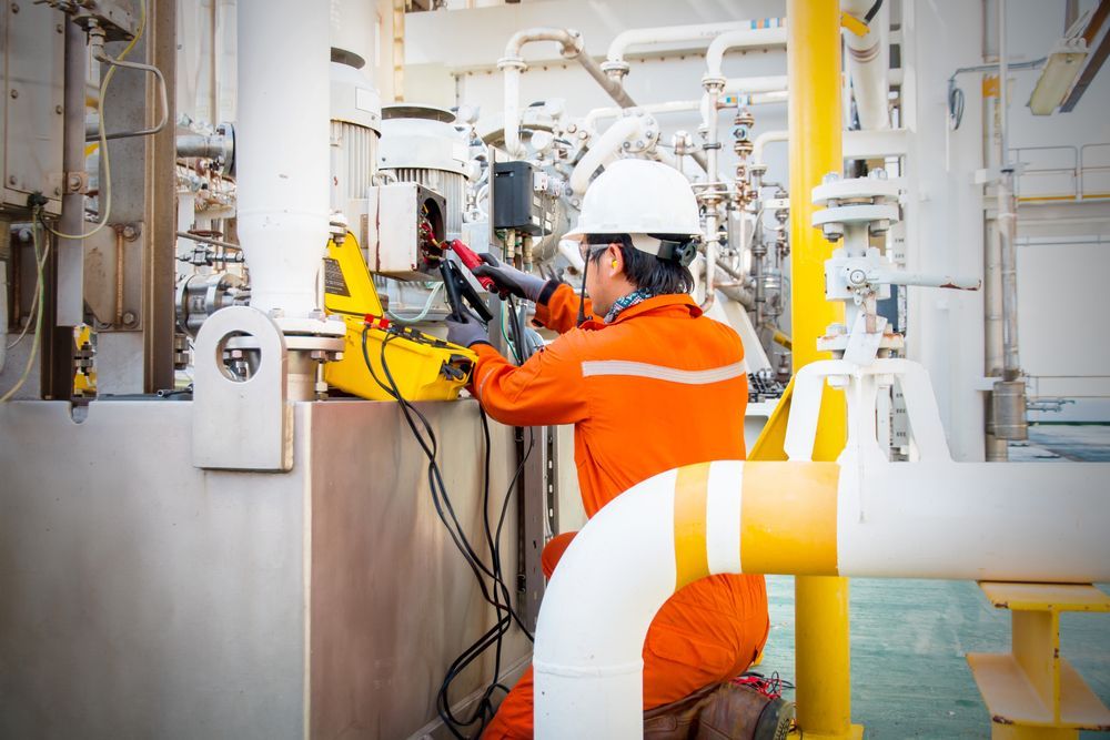 A Man In An Orange Jumpsuit Is Working On A Machine In A Factory — Keany's Electrical Service In North Nowra, NSW