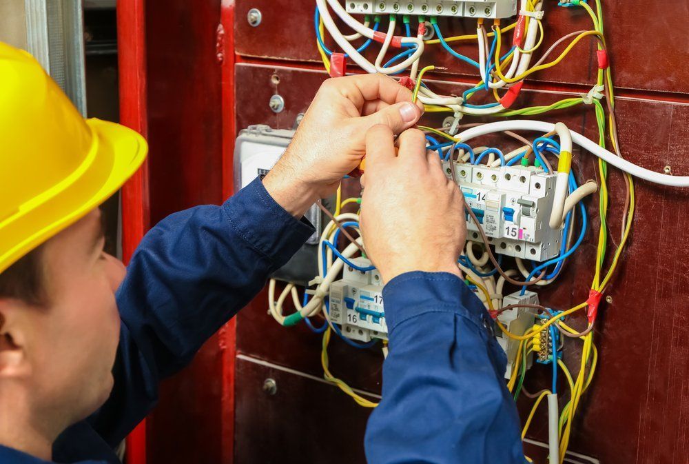 A Man Wearing A Hard Hat Is Working On An Electrical Panel — Keany's Electrical Service In North Nowra, NSW