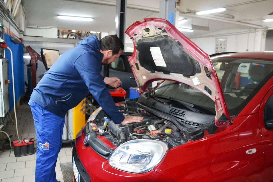 Un meccanico lavora sotto il cofano di un'auto rossa in un'officina meccanica.