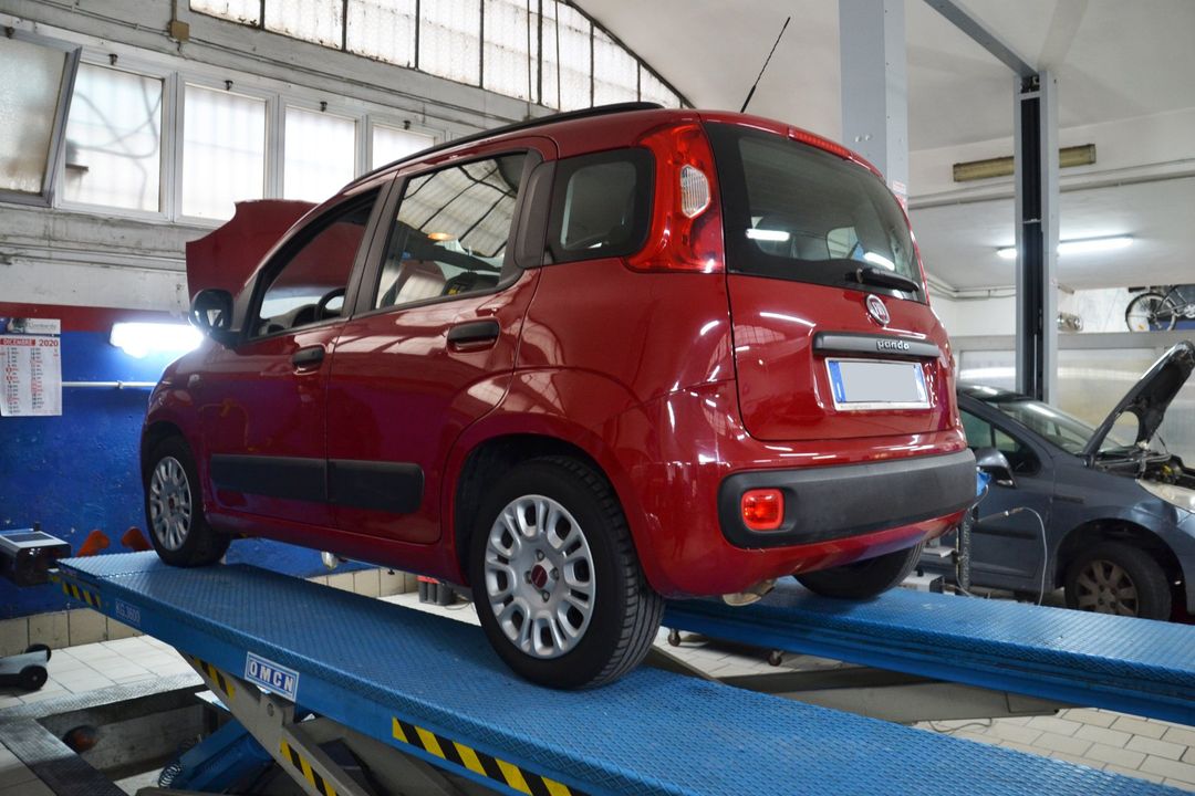Una berlina rossa su un ponte sollevatore in un'officina meccanica, con la ruota posteriore smontata.