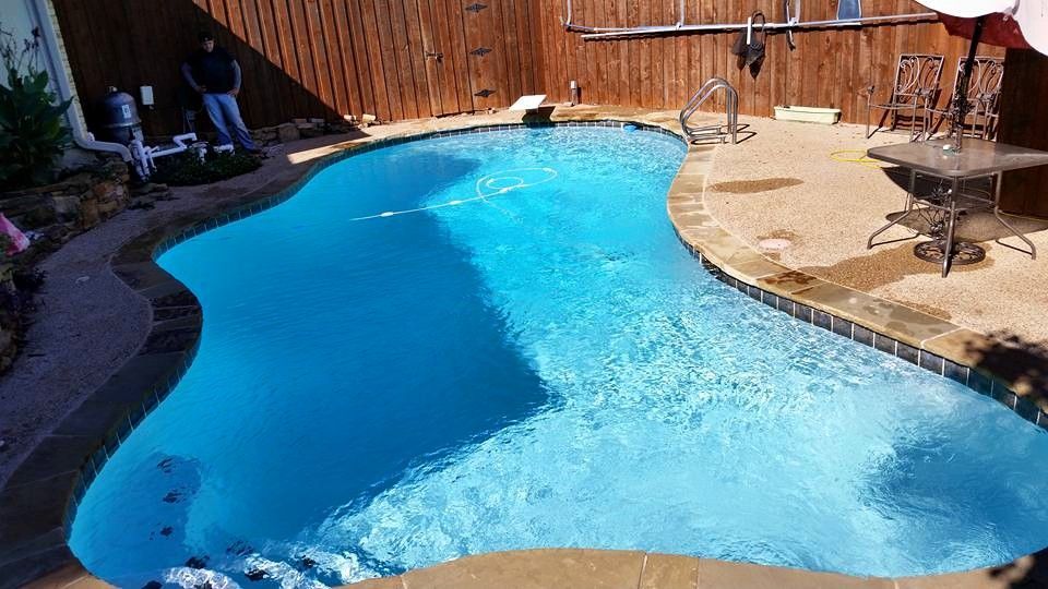 A large swimming pool is surrounded by a wooden fence and patio furniture.