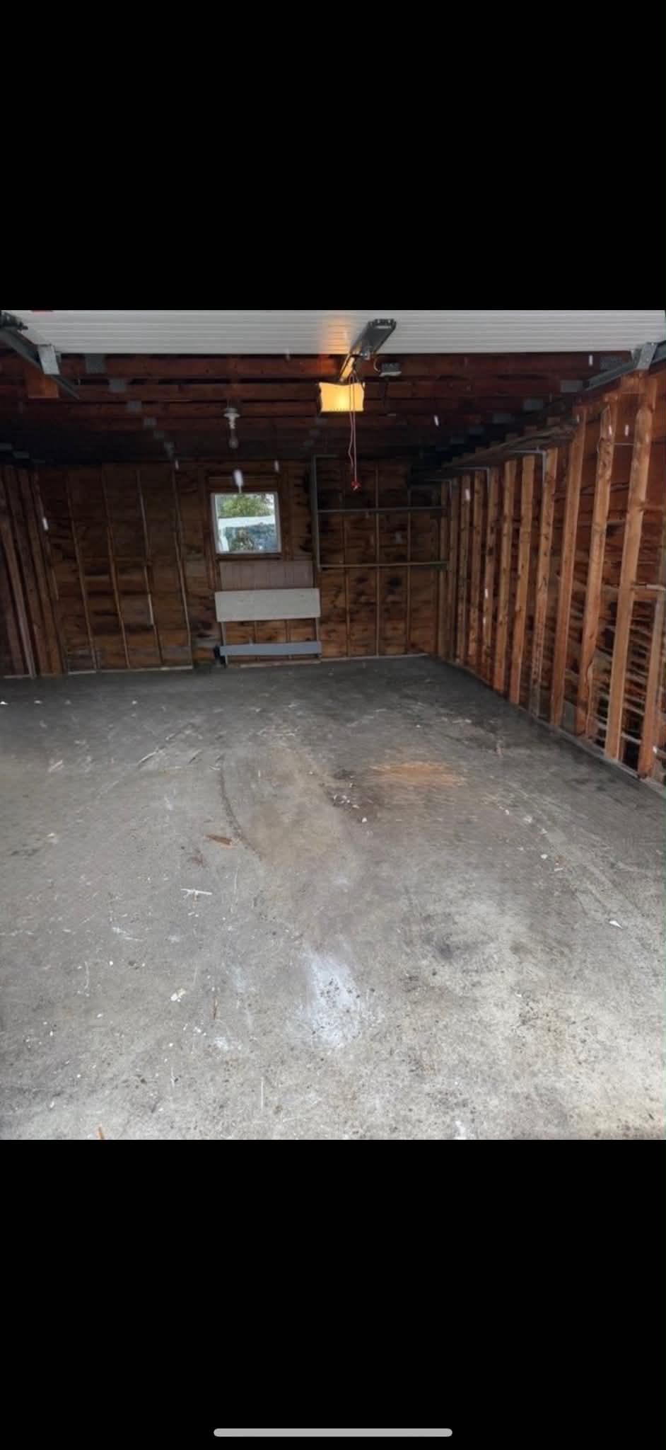 Intérieur d'un garage vide avec charpente en bois apparente, sol en béton et une petite fenêtre à l'arrière.