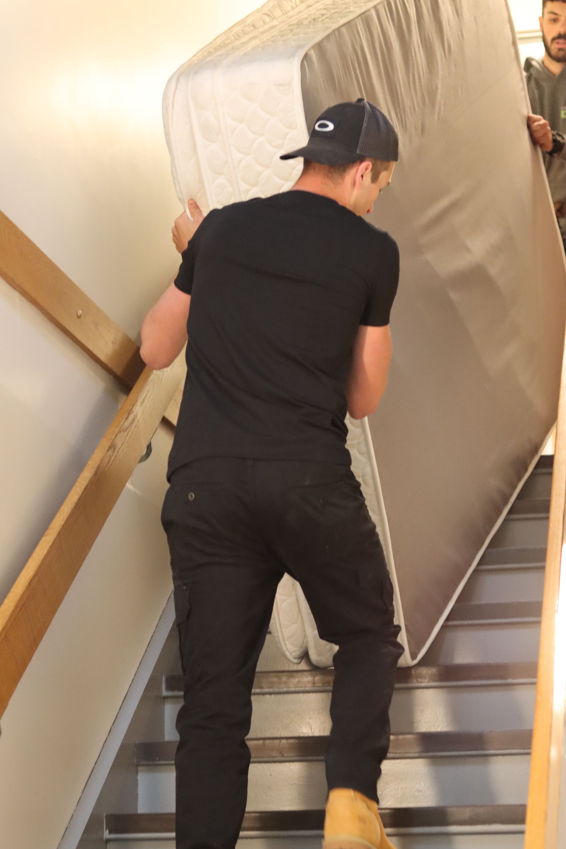 Un homme transporte un grand matelas emballé en haut d'un escalier étroit à l'intérieur.