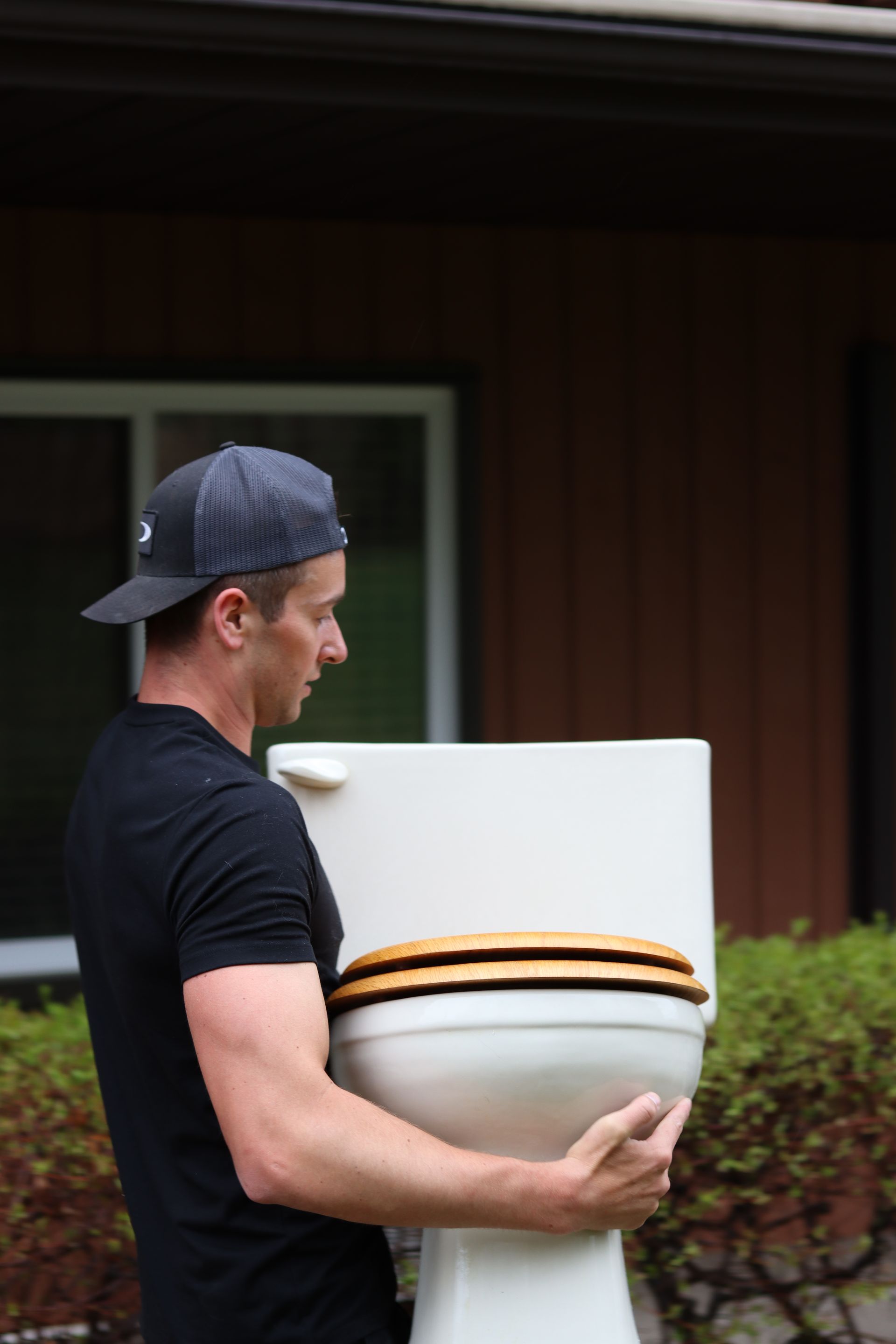 Un homme tenant une grande toilette blanche à l'extérieur, devant une maison