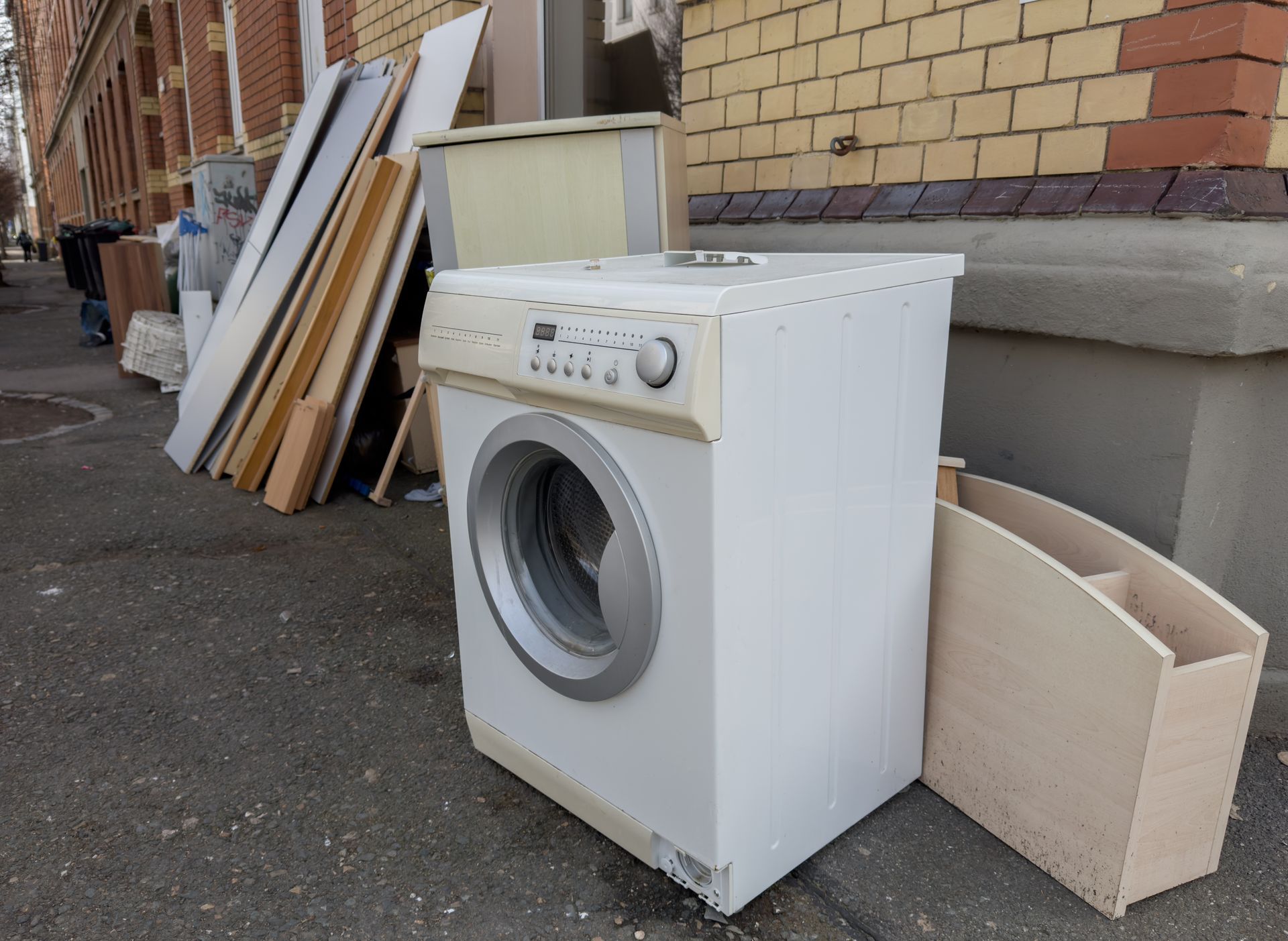 White washing machine and stacked boards by a brick wall on a sidewalk