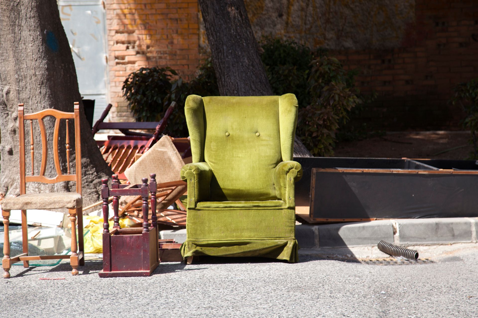 Green armchair and assorted furniture on a sidewalk in front of a brick wall and tree stump.