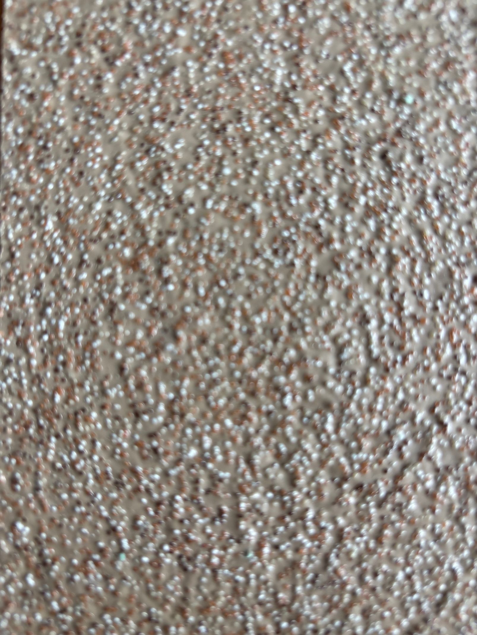 Mur beige texturé avec de petites taches foncées.