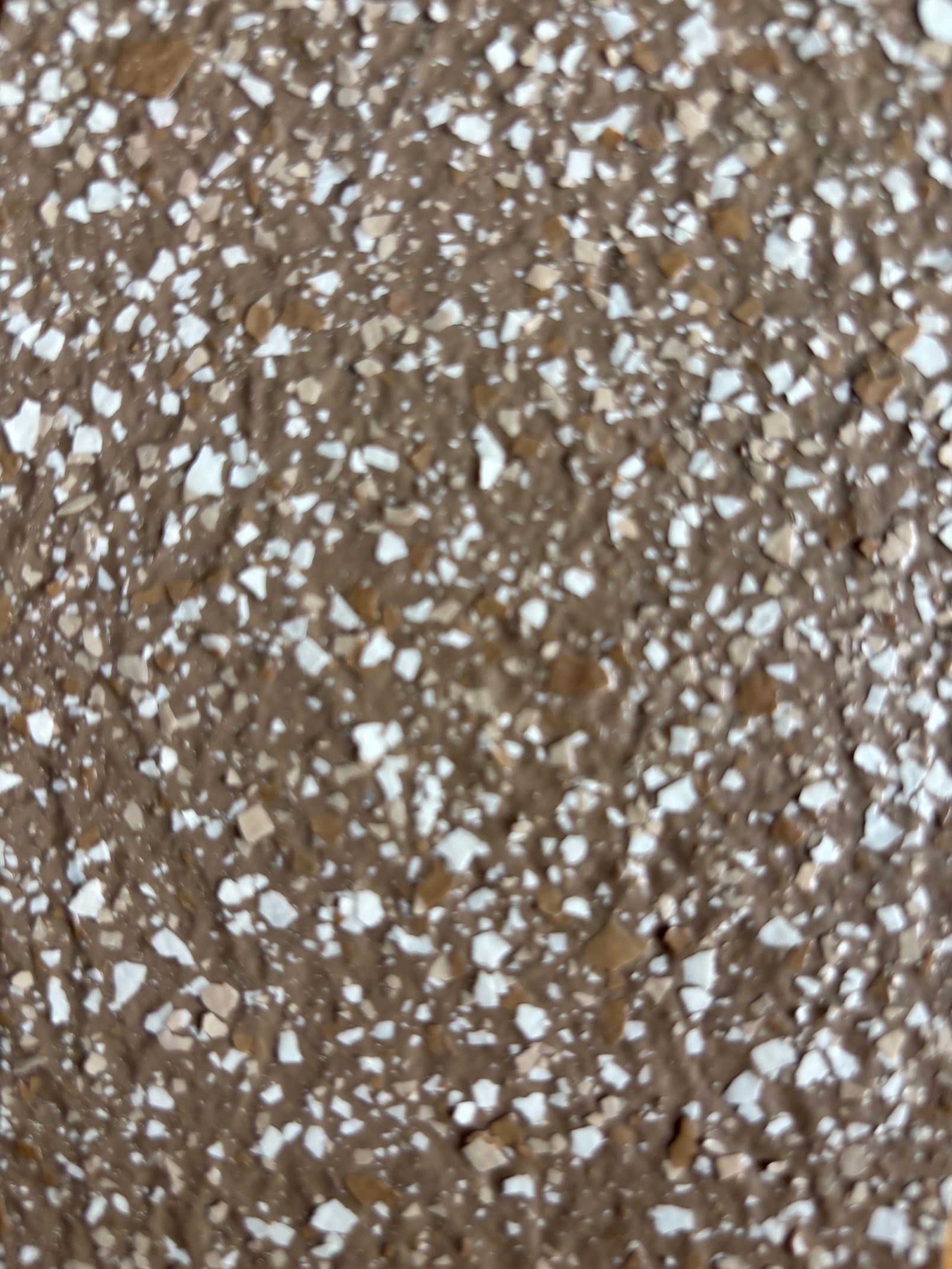 Surface texturée brune avec des mouchetures blanches et beiges incrustées.