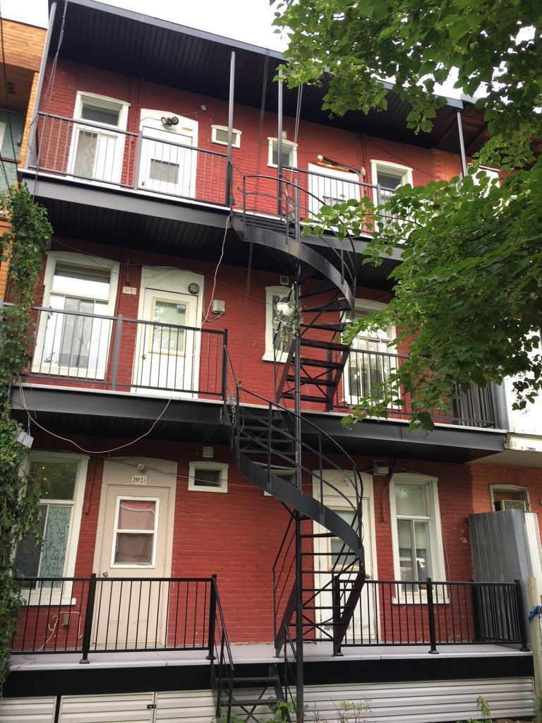 Immeuble en briques rouges avec escalier en colimaçon noir. Balcons à chaque étage.