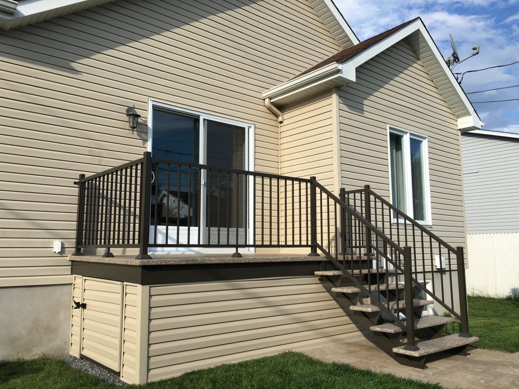 Maison beige avec porte coulissante et escalier menant à une terrasse avec rambarde noire.