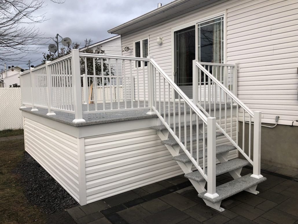 Terrasse blanche avec rambarde et escalier, attenante à une maison avec porte-fenêtre coulissante.