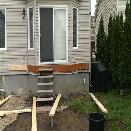 Extérieur de la maison avec porte coulissante, marches en bois et matériaux de construction.