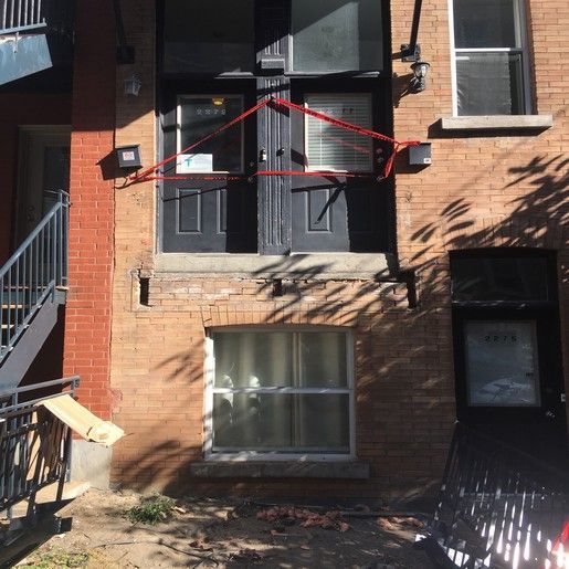 Bâtiment en briques avec double porte, fenêtres et ruban de signalisation rouge.