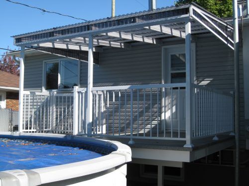 Terrasse avec rambarde blanche et porte-fenêtre couverte, jouxtant une piscine hors sol avec une couverture bleue.