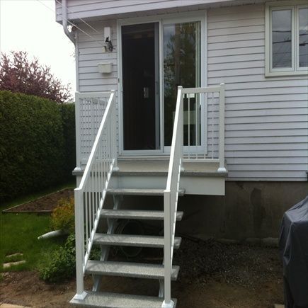 Un escalier et une rampe blancs mènent à une porte coulissante donnant sur une maison blanche.