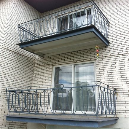 Deux balcons métalliques sur un immeuble en briques blanches. Chacun est doté d'une balustrade et de supports ouvragés.