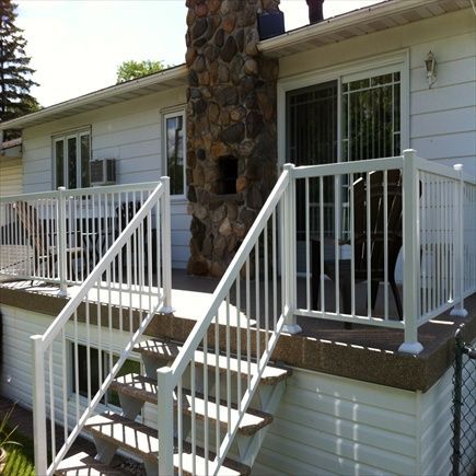 Une balustrade et un escalier blancs mènent à une terrasse avec une porte coulissante en verre et une cheminée en pierre.