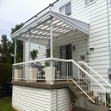 Un auvent blanc recouvre une terrasse avec une rambarde, des marches et un revêtement extérieur blancs, attenante à une maison.