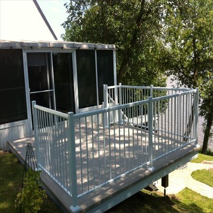 Terrasse à balustrade blanche avec véranda grillagée, donnant sur un jardin verdoyant et un plan d'eau sous un ciel ensoleillé.