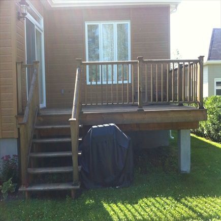 Terrasse en bois avec escalier, rambarde et barbecue couvert, attenante à une maison au bardage marron.