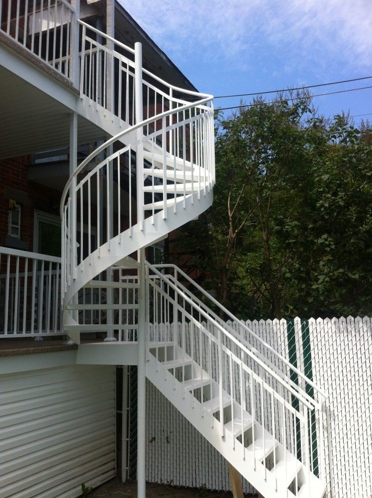 Escalier extérieur blanc en colimaçon, attenant à un bâtiment en briques.