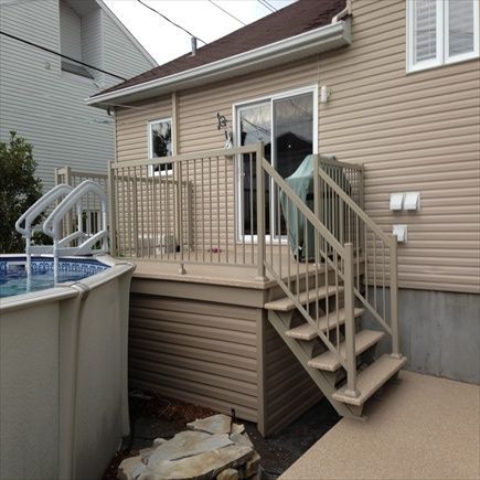 Terrasse beige avec escalier, porte coulissante en verre et piscine hors sol partiellement visible.
