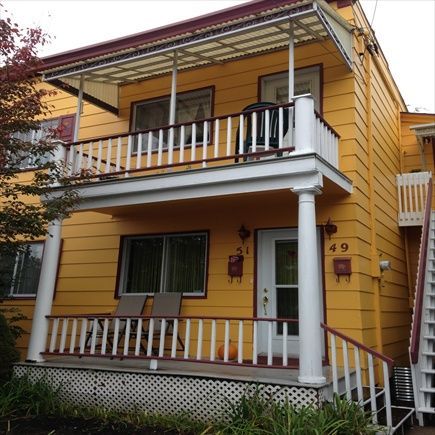 Bâtiment jaune de deux étages avec porches et balustrades blanches. Numéros 49 et 51 sur la porte. Escalier sur le côté.