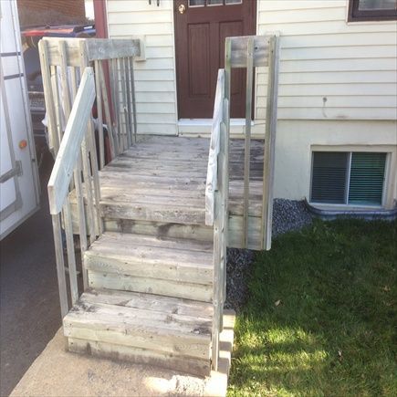 Un escalier en bois mène à une porte brune à encadrement blanc. L'escalier est muni d'une rampe et présente des signes d'usure.