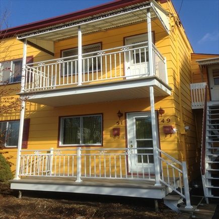 Bâtiment jaune à deux étages avec des balustrades et des portes blanches, les numéros 49 et 51 sur les portes, et un auvent rouge.