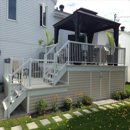 Terrasse avec gazebo, escalier, rangements et jardin. Bardage beige et balustrade blanche.