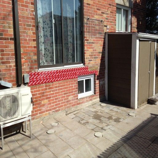 Extérieur d'un bâtiment en briques avec fenêtre, climatiseur et abri de jardin sur une terrasse.