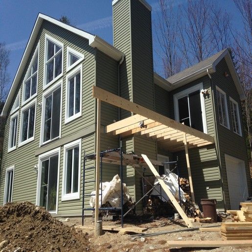 Maison en construction avec bardage vert, fenêtres blanches et pergola en bois.