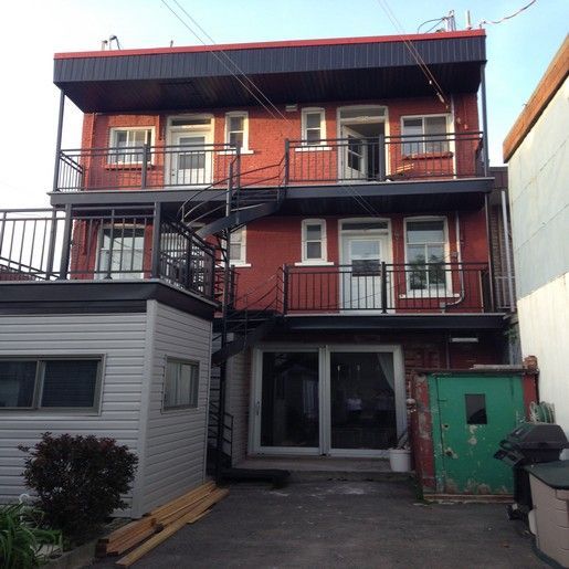 Immeuble de plusieurs étages en briques rouges avec balcons en métal noir et escalier en colimaçon.