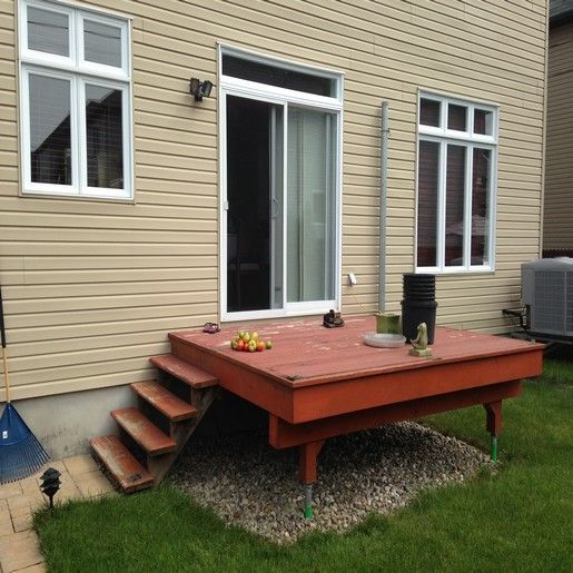 Terrasse avec escalier donnant sur une porte-fenêtre coulissante. Revêtement extérieur beige, pelouse, sol en gravier.