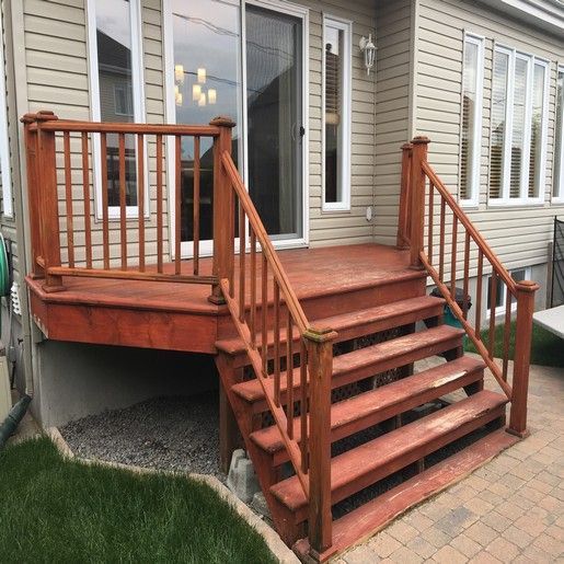Terrasse en bois rouge avec escalier et rambarde, à l'extérieur d'une maison.