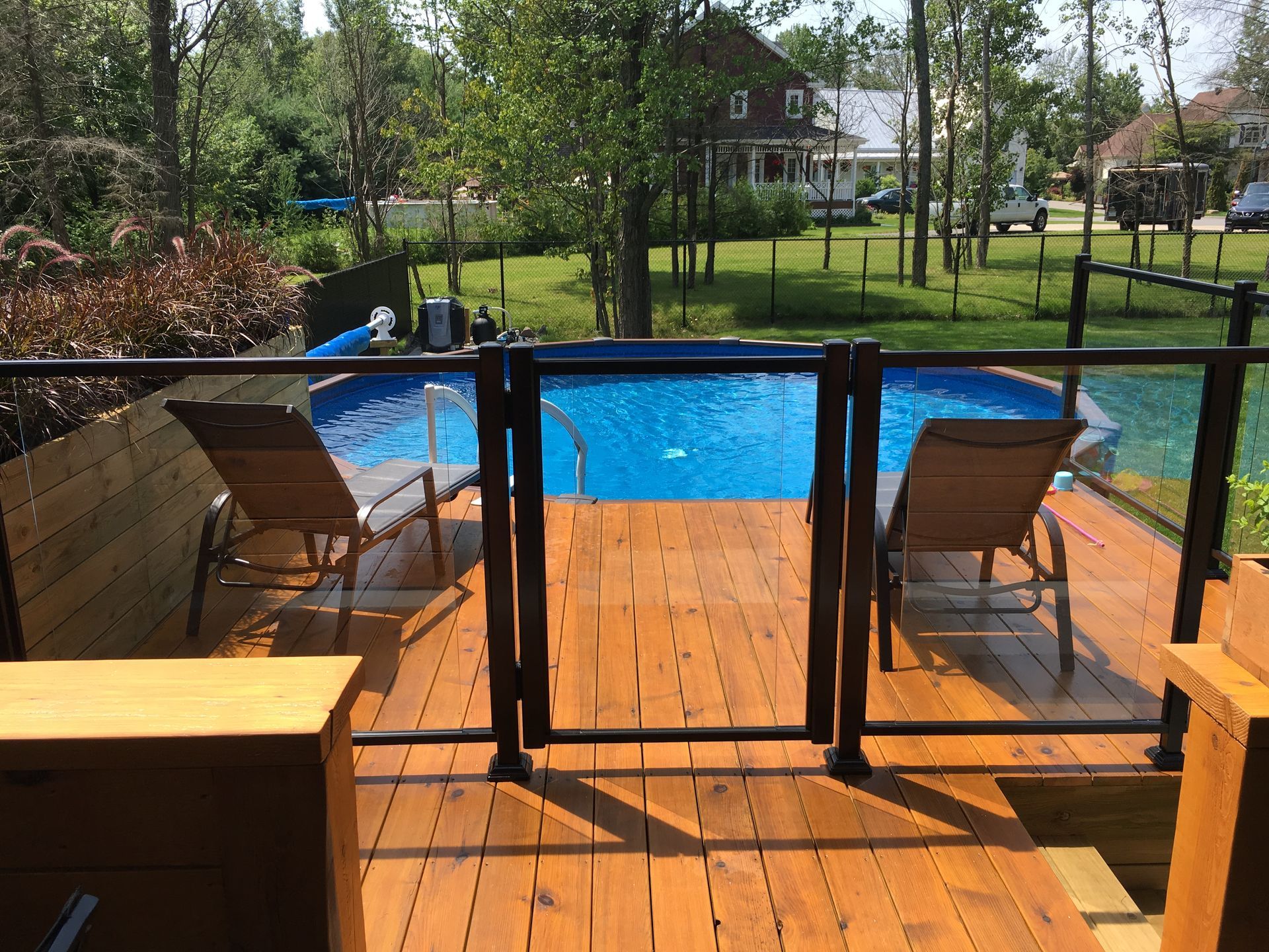 Terrasse avec piscine hors sol et barrière de sécurité en verre. Deux chaises longues font face à l'eau, cadre extérieur ensoleillé.